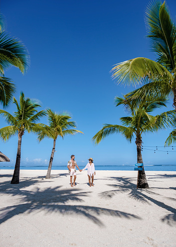 Le Morne beach Mauritius Tropical beach with palm trees and white sand blue ocean couple men and woman walking at the beach during vacation