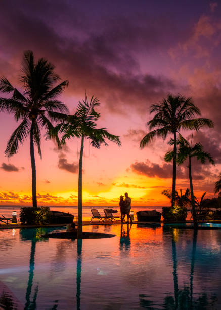 couple men and woman watching sunset on a tropical beach in Mauritius with palm trees by the swimming pool, Tropical sunset on the beach in Mauritius stock photo