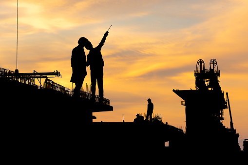 Silhouette of Engineer and foreman worker checking project at infrastructure construction site, construction site at sunset in evening