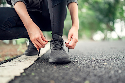 Close up - Running shoes runner woman tying laces for summer run in forest park. Jogging girl exercise motivation health and fitness exercise. copy space.