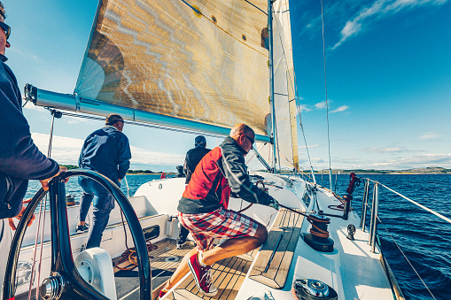 Bodrum,Mugla, Turkey. April 01, 2023: sailor team driving sail boat in motion, sailboat wheeling with water splashes, mountains and seascape on background. Sailboats sail in windy weather in the blue waters of the Aegean Sea, on the shores of the famous holiday destination Bodrum