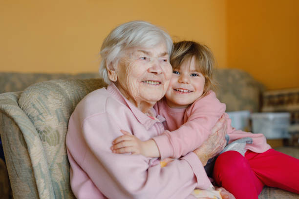 Beautiful toddler girl and great-grandmother hugging together at home. Cute child and senior woman having fun together. Happy family indoors stock photo