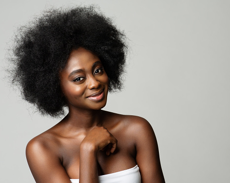 Dark Skinned Beauty Model with Afro Hair. Happy African Woman with Curly Volume Hairstyle over White Background. Black Skin Care and Healthy Cosmetology