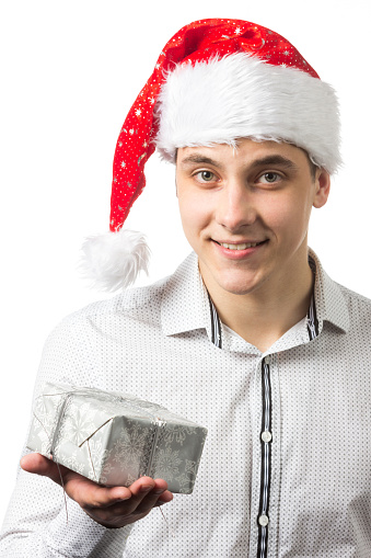 Young handsome man wearing a Santa hat over white background surprised, showing and pointing something that is on her hand. High quality photo