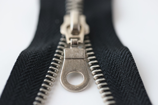 Closeup macro shot of open black brass zipper isolated on white background. Metal zipper is connected to zipper and is pulled by slider of zipper concept