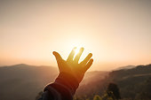 Young man hand reaching for the mountains during sunset and beautiful landscape