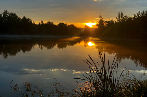 Sun sets over the horizon above calm lake on summer evening nature landscape