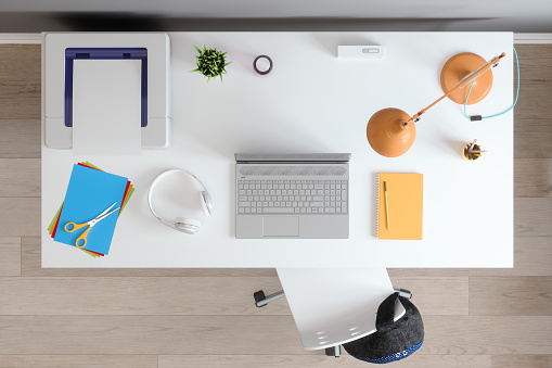 Top View Of Workspace With Laptop, Computer Printer, Headphones, Desk Lamp And Backpack