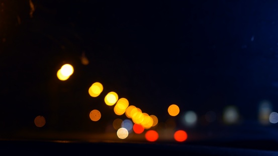 View from the front window of the car on the night road with blurry lights of passing cars and lighting lamps. Out-of-focus view of an unrecognizable road at night with beautiful bokeh.