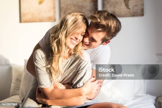 Happy Young Couple Relaxed At Home On Bed Stock Photo - Download Image Now - Bed - Furniture, Young Couple, Falling in Love