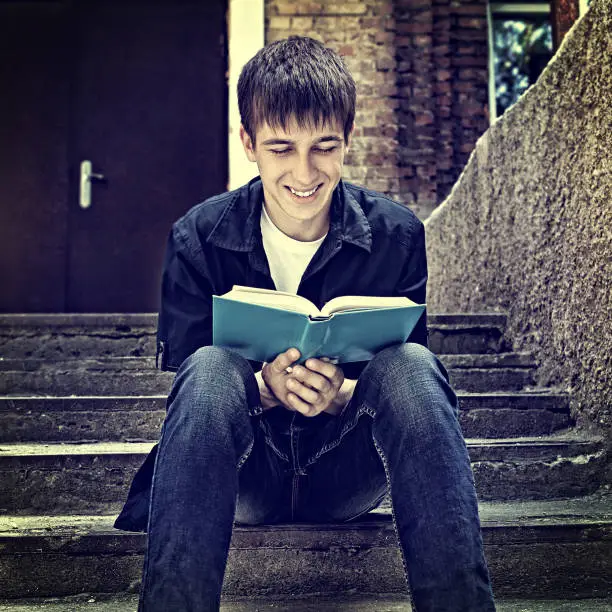 Toned Photo of Cheerful Teenager read the Book on the City Street