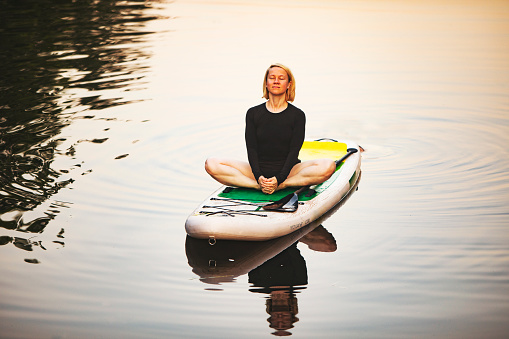Young woman practicing yoga on sup at sunset