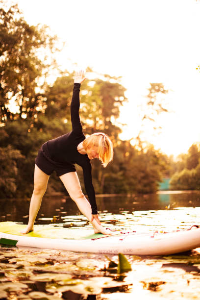 istock Young woman practicing yoga on sup at sunset 1412160307