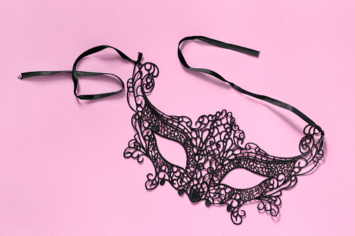 Black lacy carnival mask on pink background