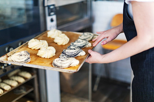 Baker putting baking tray with buns into oven