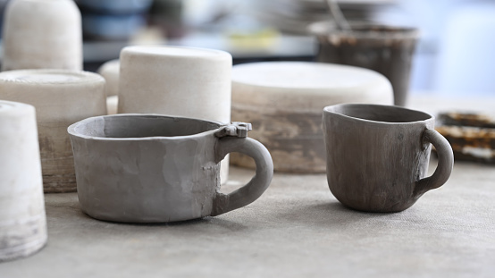 Set of handmade ceramic crockery and pottery shaping tools on wooden table in creative studio.