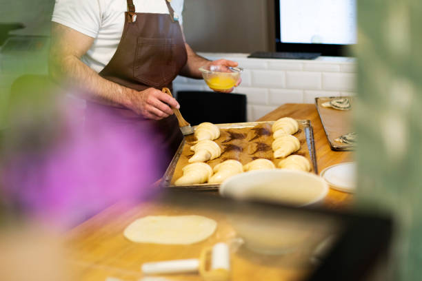 homme préparant des croissants dans une boulangerie, les mains serrées avec du beurre - cooked in a row traditional culture indoors photos et images de collection