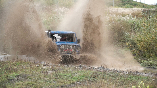 A car is driving in the countryside participating in the race and crossing wide dirty puddle, making giant water splash, motor sport concept. Vehicle on the track, off-road racing.