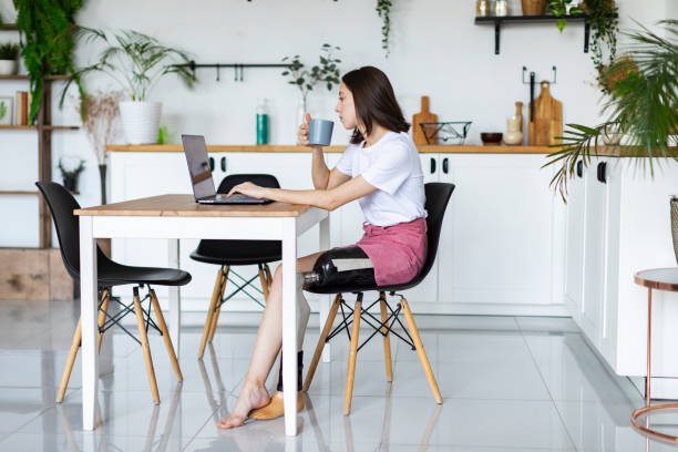 istock Young woman amputee with prosthesis using laptop at kitchen 1412165871