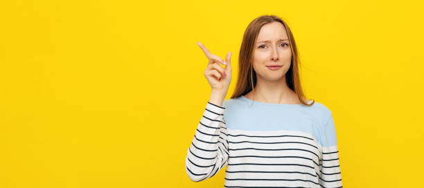 istock Impressed, happy attractive girl with fair-haired pointing looking upper left corner at advertisement, price offer. Indoor studio shot on yellow background 1412168096