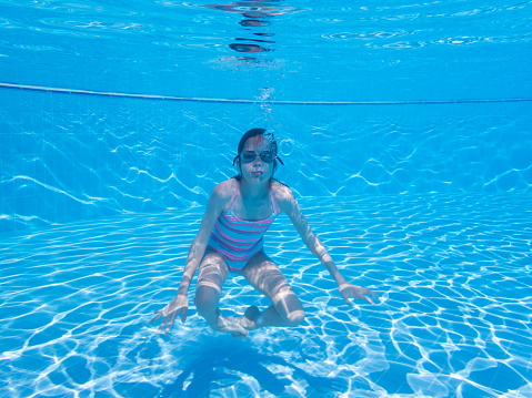 Female with goggles relaxing underwater in the blue waters of a swimming pool. Sport, recreation, lifestyle concept.