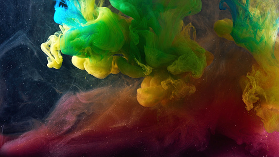 Colorful rainbow paints being squeezed into water on black background. Colored clouds moving slowly underwater and mixing.
