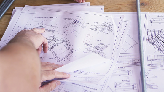 Close up view on hands pointing at technical drawings lying on the table. Man hands indicating some details in papers, constructors at work