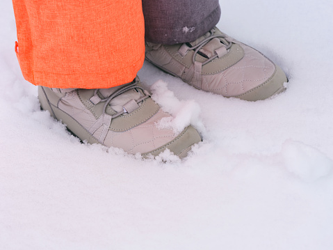 A close-up shot of child feet in winter shoes standing on snow.