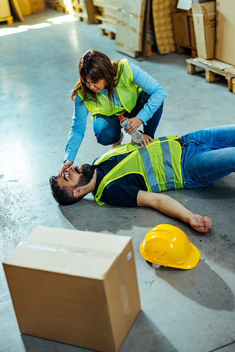 Warehouse Worker helping unconscious worker lying at industrial factory floor.