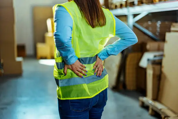 A warehouse worker in pain holding backs and making painful grimace.