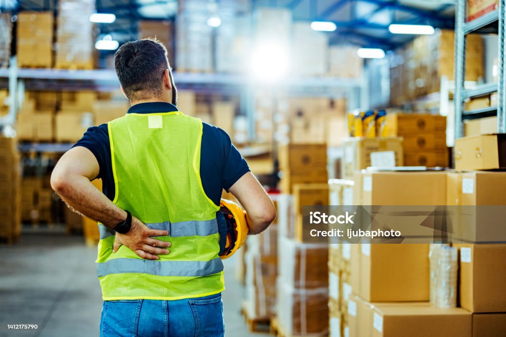 A warehouse worker having back pain and rubbing it. Physical Injury Stock Photo