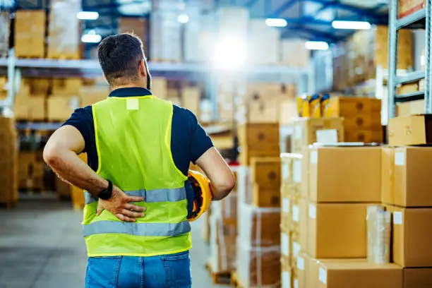 Photo of A warehouse worker having back pain and rubbing it.