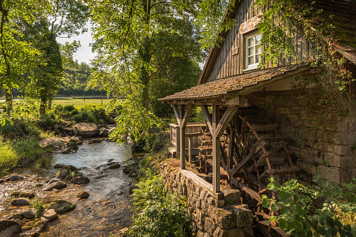 A wooden water wheel or watermill turbine milling, grinding, turning, and generating power, perhaps as a traditional alternative energy source. Positioned against the stone wall of a cottage building exterior, located in St. Paul, Minnesota, USA.