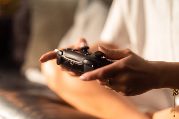 Woman playing video games at home in her living room. She is sitting on her sofa with a video game controller in her hand, eyes locked on the TV.