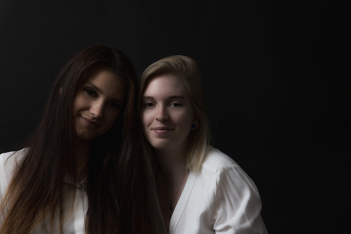 Low key portrait of two young women posing for the camera in the studio. Horizontally.