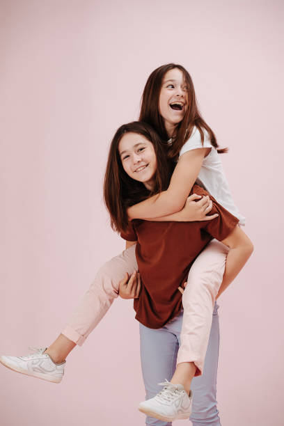 istock Smiling joyful twin sisters playing. One is riding on another's back. Over pink 1412184019