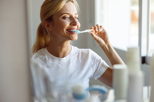 Close up. Cheerful young blonde female brushing teeth with toothbrush at mirror. Take care of teeth.