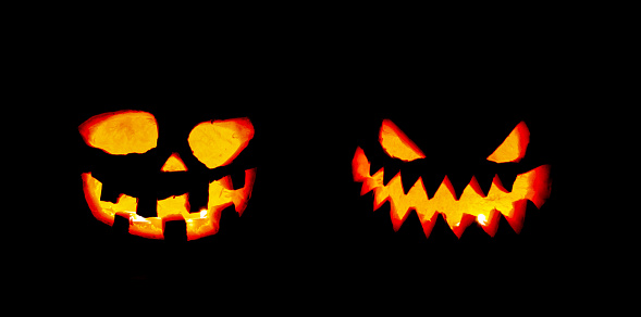 Two halloween pumpkin heads illuminated by candles from inside on black background