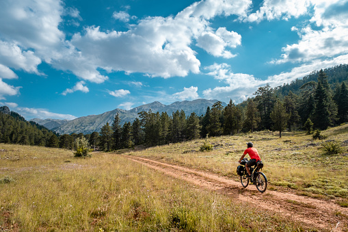 Taken from the rear view. Forest and mountain scenery. Cloudy open air, dirt road. Adherent to the adventurous spirit, high vitality..He is 30 years old, doing a camping bike tour. There are various bags on his bike, around 60 liters in total.Mediterranean region Antalya, Taurus mountains.