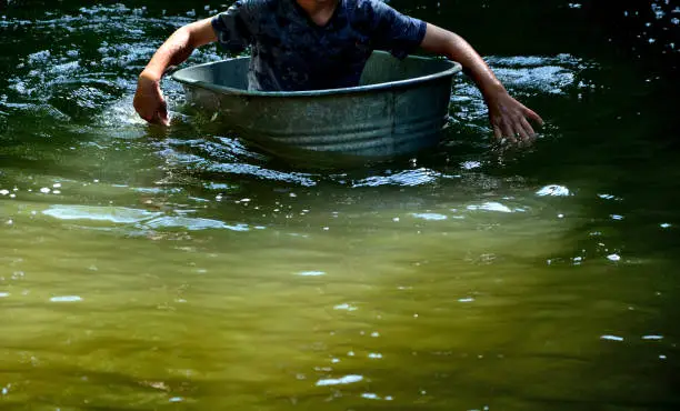 Photo of The boys sail on a boat made of old tin, tubs, a bucket, a barrel, a bowl, an oval-shaped flower pot. they fall on the river with their hands. they are children's adventures in the village