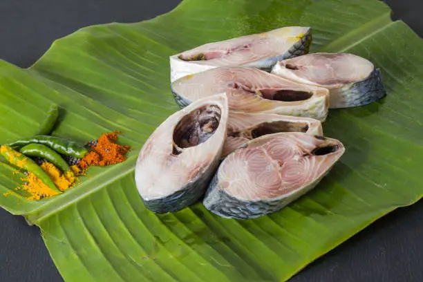 Photo of Raw hilsa fish cut into pieces kept on banana leaf for cooking. Shot taken in studio with copy space background and spices.