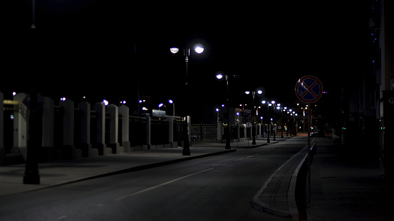 Beautiful and calm atmosphere of the summer night in big city, dark street with many shining lanterns. Empty road and sidewalk.