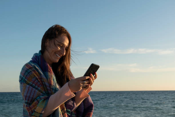 istock woman using her smartphone on a cold day at the beach 1412194495