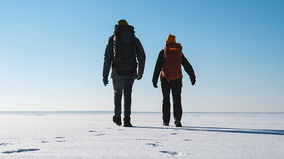 The two tourists with backpacks traveling through the snow field