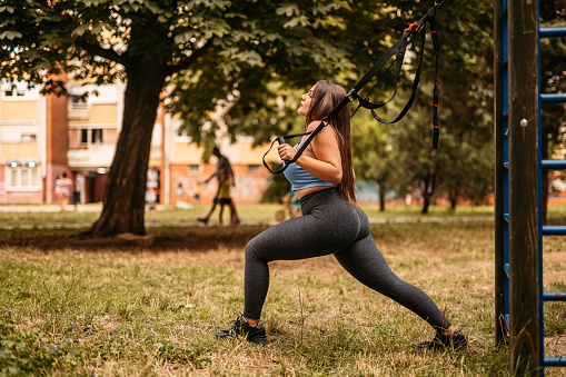 Beautiful plus size young woman exercising in park during the day. Using a resistance band.