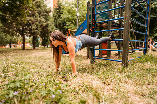 Beautiful plus size young woman exercising on monkey bars in park during the day.