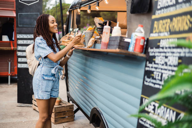 Afro girl buying potato at the fast food truck Beautiful African American young woman buying fast food at the food truck on the street street food stock pictures, royalty-free photos & images