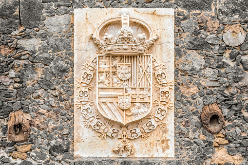 Puerto de la Cruz, Spain - November 25, 2021: Coat of arms of the Castillo de San Felipe Fortress in Puerto de la Cruz. Antique marble bas-relief on a stone wall