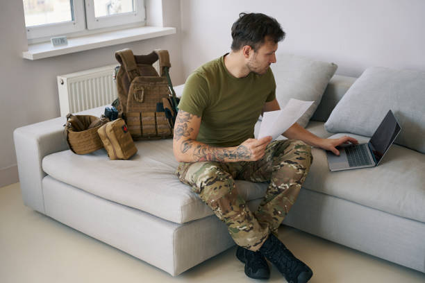 istock Soldier working on laptop online while holding paperwork 1412206459