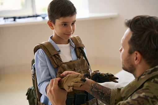 Child looking at his father while he zipping up glove on his hand during military gear training